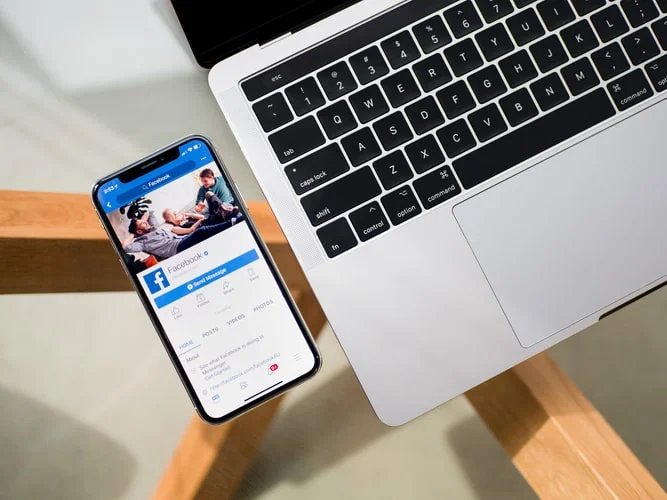 Facebook Ads: celular revisando la red social Facebook al lado de un computador.